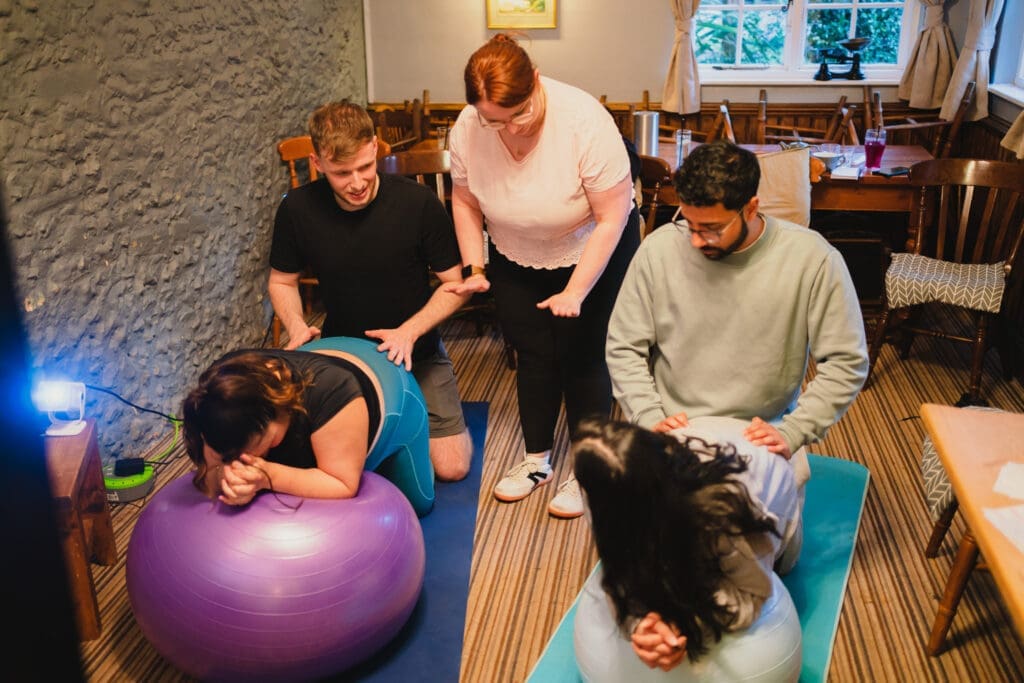 Antenatal class in Caterham with a tutor demonstrating birthing positions to students using exercise balls.
